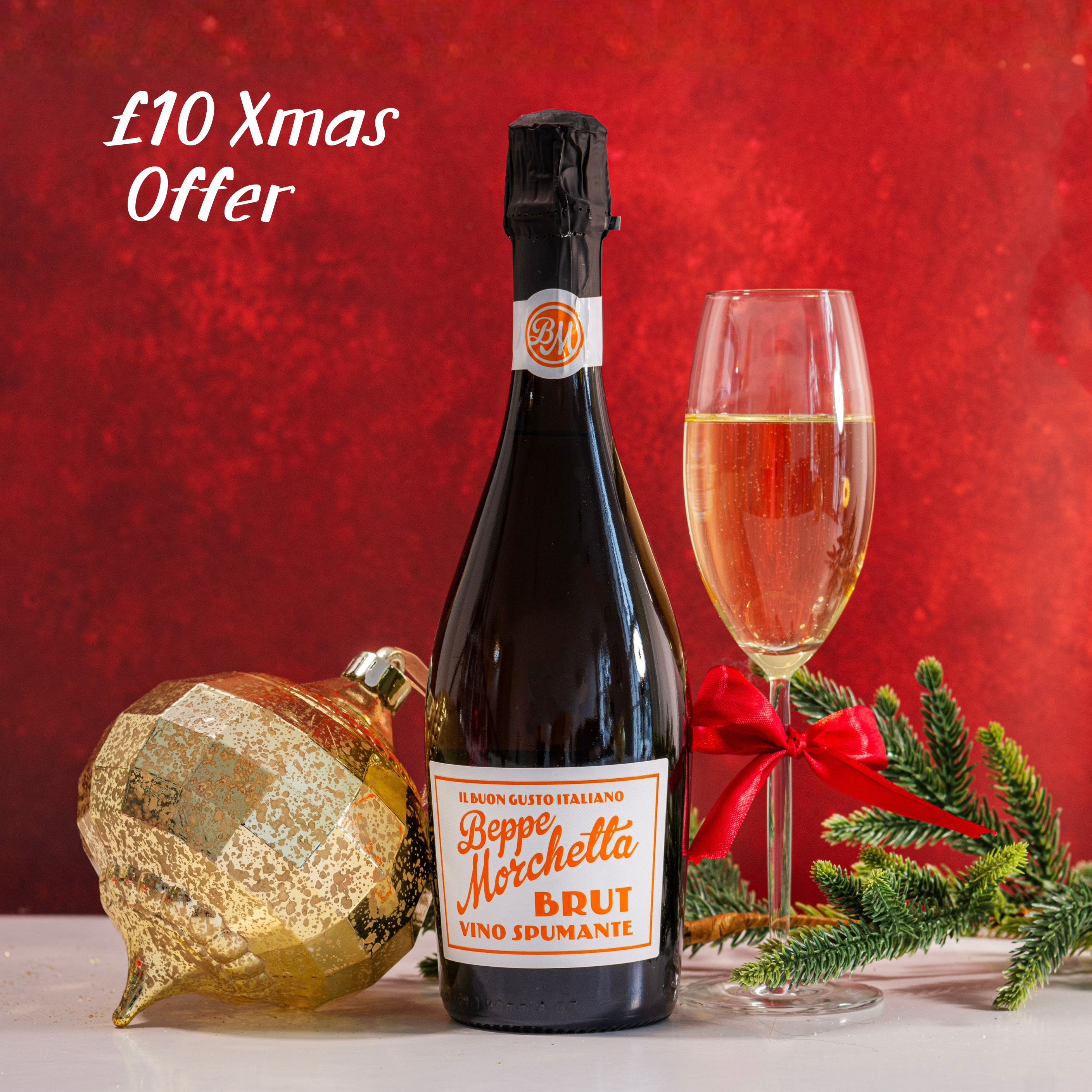 Bottle of Beppe Morchetta Spumante with a glass of fizz, Christmas decorations, and a red background. Christmas offer.